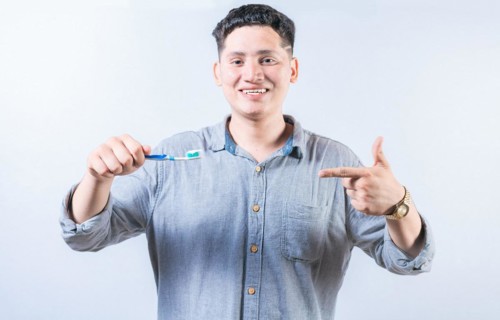 Man holding and recommending a toothbrush. Smiling guy holding and pointing at toothbrush isolated.