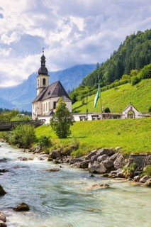 Parish church of St Sebastian by a river in an idyllic Alpine landscape with mountains and forests