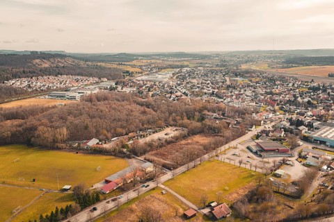 Village with winding roads surrounded by trees, fields and rolling hills under a cloudy sky,