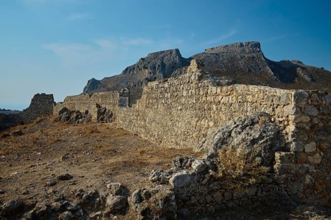 Stone ruins in an arid landscape with mountains in the background under a clear sky, fortress