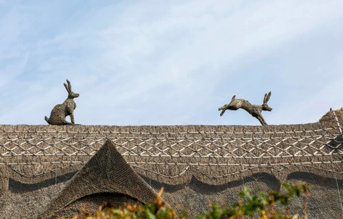 Figures of thatch hares running along ridge of thatched cottage roof, Sutton, Suffolk, England, UK