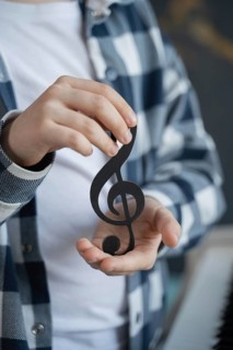 A young boy in a patterned shirt holds a black treble clef symbol delicately in his hands,
