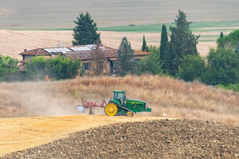 Tractor plows a dried harvested grain field in a typical Tuscan landscape in Crete Senesi in
