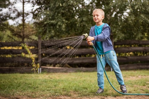 Young boy watering grass in the garden