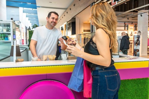 Smiling vendor processing a cashless payment for a customer purchasing ice cream, holding shopping