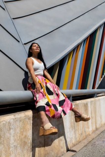 A woman in a vibrant, colorful outfit sits gracefully against a striking backdrop of modern