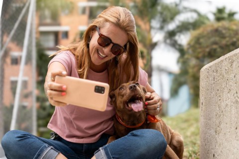 A happy woman wearing sunglasses smiles as she takes a selfie with her adoring dog