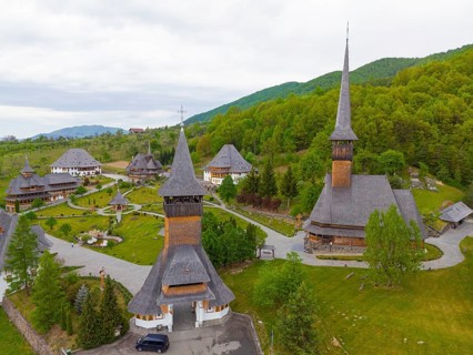 Monastery with wooden churches and steep roofs surrounded by lush green forest, aerial view,