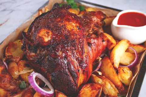 Baked pork knuckle, with potato slices, on a tray, with red sauce, homemade, no people, light