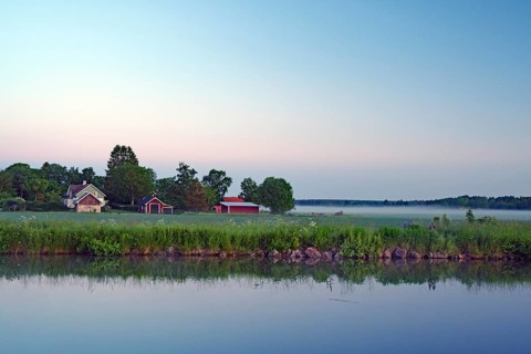 Morning light over a quiet lake with houses and fog in the surrounding countryside, Göta Canal,
