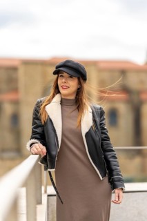 Portrait of a fashionable woman posing in a city environment, wearing a black cap, leather jacket,