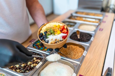 Person in black gloves holding colorful acai bowl with kiwi, blueberries, strawberries and banana
