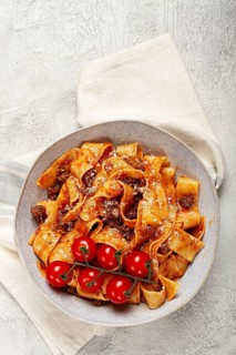 Pappardelle pasta with bolognese sauce, topped with parmesan cheese and cherry branch, homemade, no