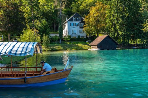 Traditional pletna boat waiting for tourists on the beautiful lake bled, with a villa and boathouse