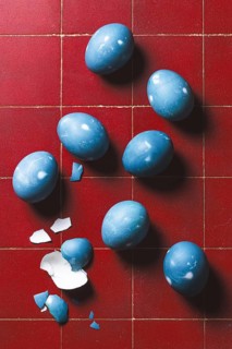 From above, a collection of blue Easter eggs on a red tiled floor, some whole and one broken with