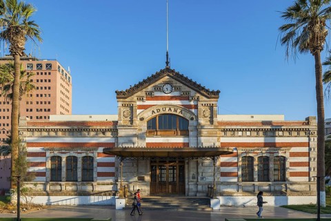 Historic customs building in General Manuel Baquedano Park between palm trees, city of Arica, Chile