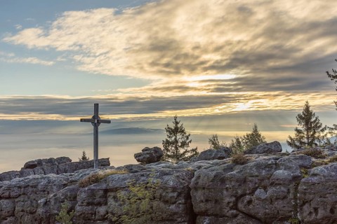 Silhouette of the summit of Mount Töpfer with summit cross, behind it morning sky with clouds and