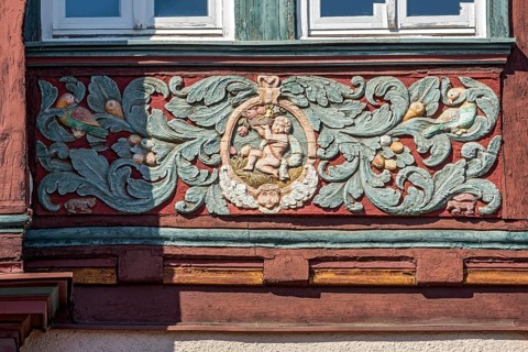 Colourfully painted carvings, medallion with putti, paradise, floral ornaments, half-timbered house