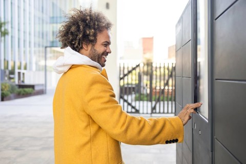 A cheerful man with afro hair, wearing a yellow coat, interacting with a touchscreen panel in an