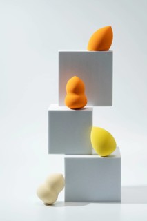 A set of vibrant cosmetic sponges in various shapes and hues is creatively displayed on stacked