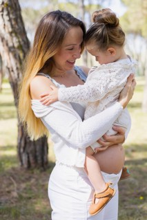 A pregnant woman joyfully embraces her young daughter in a serene outdoor setting. The scene