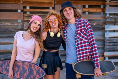 Three young skaters smiling and posing together with their skateboards in front of a rustic wooden