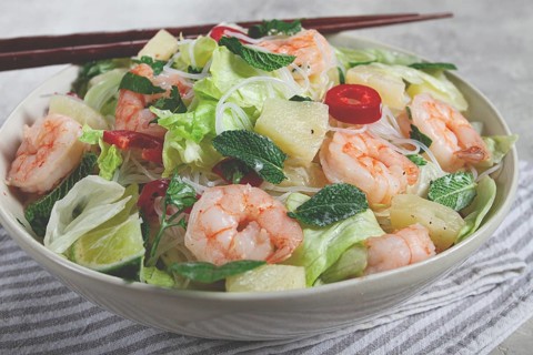 Thai salad with shrimp and rice noodles, pineapple slices, coriander and mint leaves, on a white