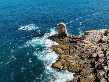Aerial view of steep granite rocks with a rock tower at Pointe du Raz on the stormy Breton coast,
