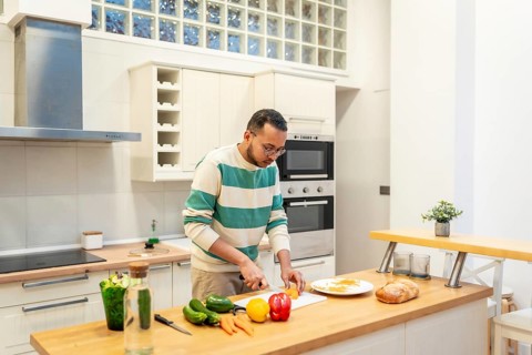 Middle aged man chopping fresh vegetables on a wooden board in a bright modern kitchen, preparing a
