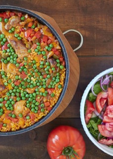 Close up view from above of paella and tomato salad. Rice with pork and chicken, vegetables and