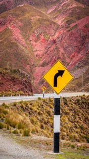 A road sign indicating a curve stands before stunning red-striped mountains. Captured in the