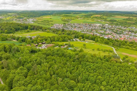 Aerial view of a green landscape with forests and a village in the background under cloudy sky,