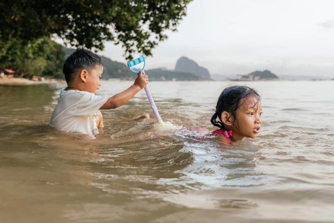 Two children play in the shallow waters of a Philippine beach. A child with short hair holds a toy,