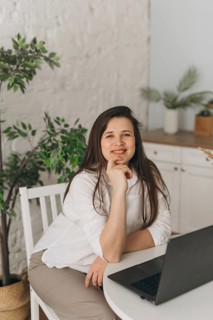A nutritionist sits at a table with a laptop, surrounded by green plants. The setting is a modern,