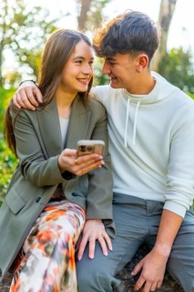 Smiling young couple sitting together, sharing a moment while looking at a smartphone, surrounded