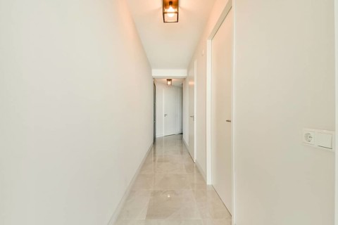 A bright, minimalist hallway with white walls and doors, featuring sleek tiles and modern pendant