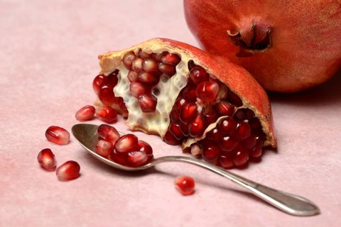 Opened pomegranate and pomegranate seeds in a spoon, Punica granatum