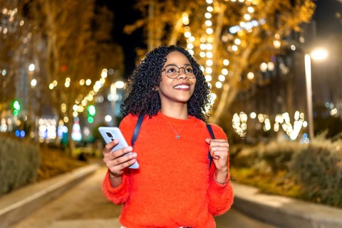 Smiling student walking through a beautifully decorated city at night, using her smartphone to