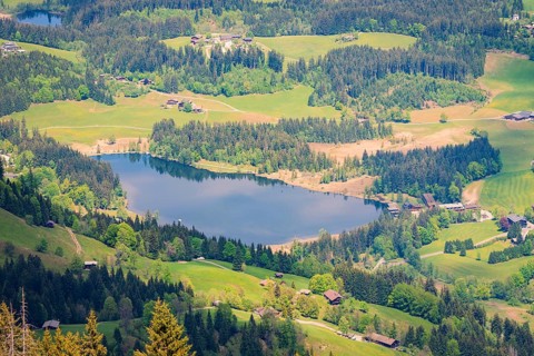 A quiet lake surrounded by forest and small villages in a hilly landscape, Hahnenkamm, Kitzbühel,