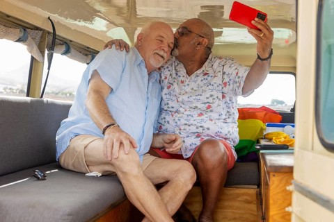 Elderly gay couple sharing a tender moment while camping inside their off-road vehicle. One man