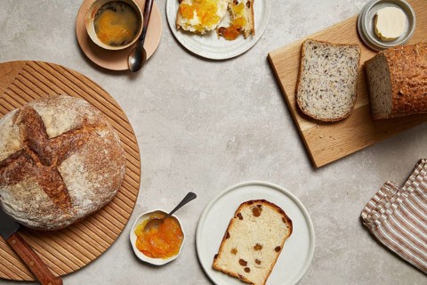 Overhead view of a breakfast setting featuring rustic bread, butter, marmalade, and coffee. Slices