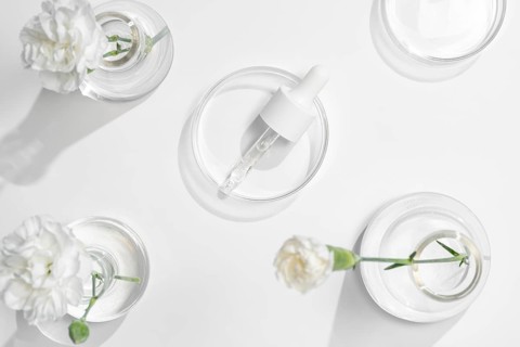 A top view of skincare laboratory equipment with serums and fresh flowers in petri dishes,