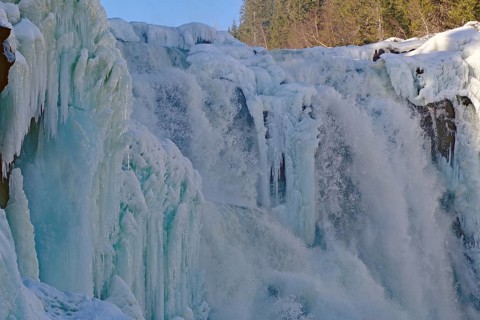 Frozen waterfall surrounded by snow-covered trees and ice formations, winter, Sweden's highest