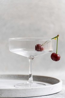 A ripe cherry delicately dangles off the edge of a clear glass, set against a textured concrete
