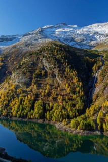 The Galgenbichl reservoir with a mountain forest in fall foliage on a bright sunny morning. Seen