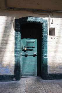 Massive green prison door with padlock surrounded by old stonework, Kilmainham Gaol Prison, Dublin,