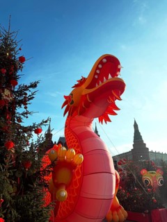 A giant red dragon figure stands tall among decorated trees during a Chinese New Year celebration,