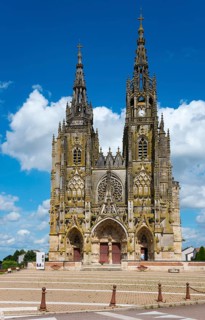 Imposing Gothic church with soaring towers and detailed architecture against a clear blue sky,