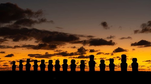 Moai statues in silhouette against orange morning sky with clouds, Ahu Tongariki, Easter Island,