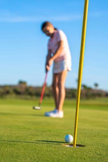 Vertical photo with focus on golf hole while girl playing on the background